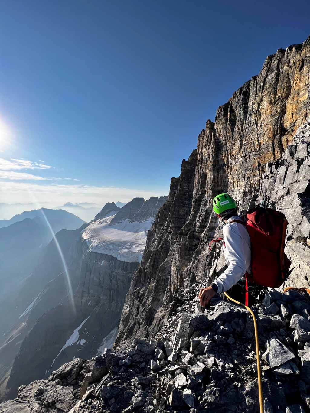 An alpine climbing in the Alberta Rocky Mountains looking at the sunrise while sitting on a ridge