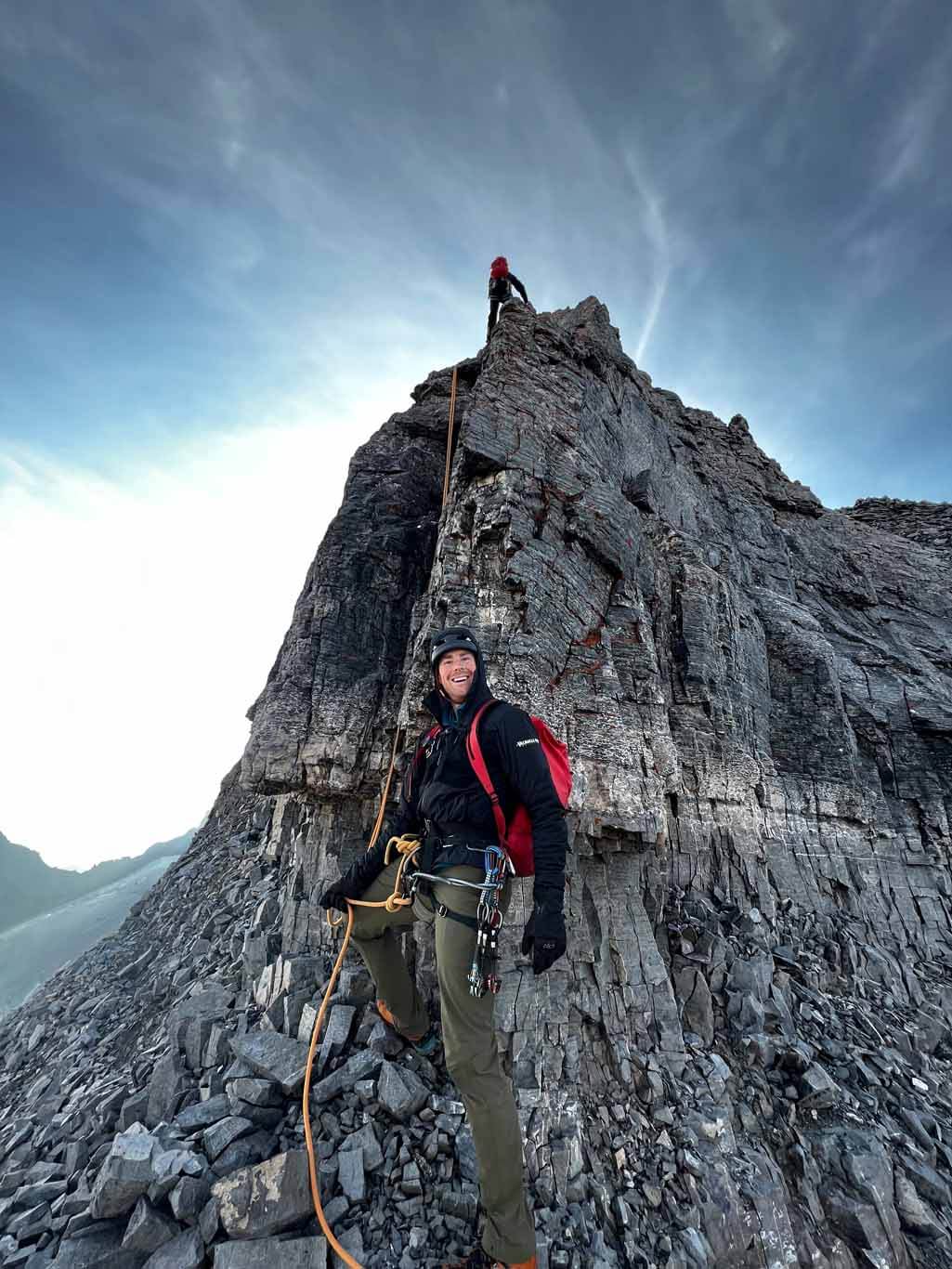 Tim Taylor guiding a client alpine climbing who is summiting a ridge line in the Alberta Rocky Mountains
