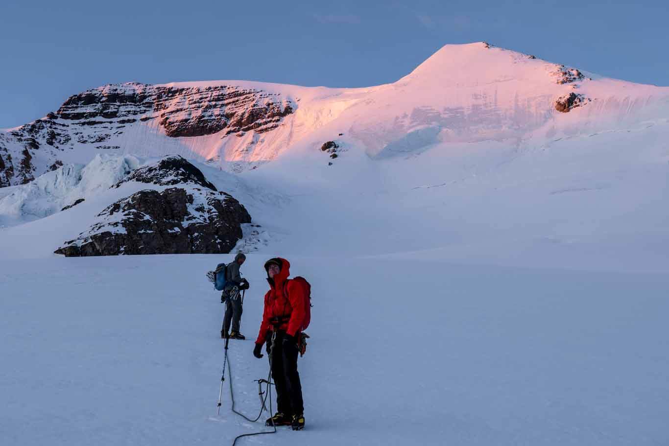 Tim Taylor guiding a client while alpine climbing in the Alberta Rocky Mountains with morning sun breaking on the ridge