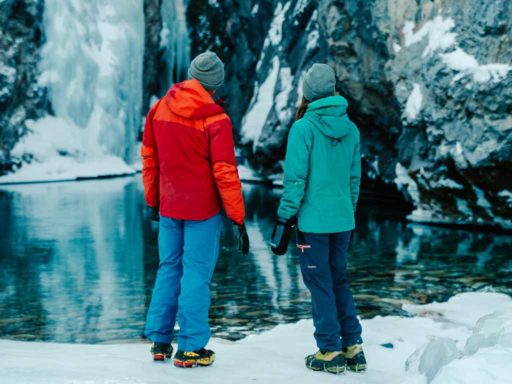 People looking a frozen waterfall dropping into a flowing river in the David Thompson Corridor, near Nordegg Alberta